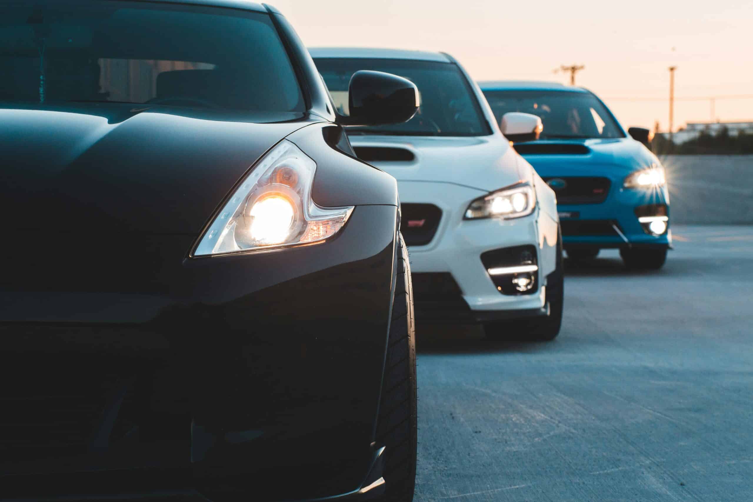 Real Cost of Car Ownership. Three modern cars parked on the road at sunset with city skyline in background.